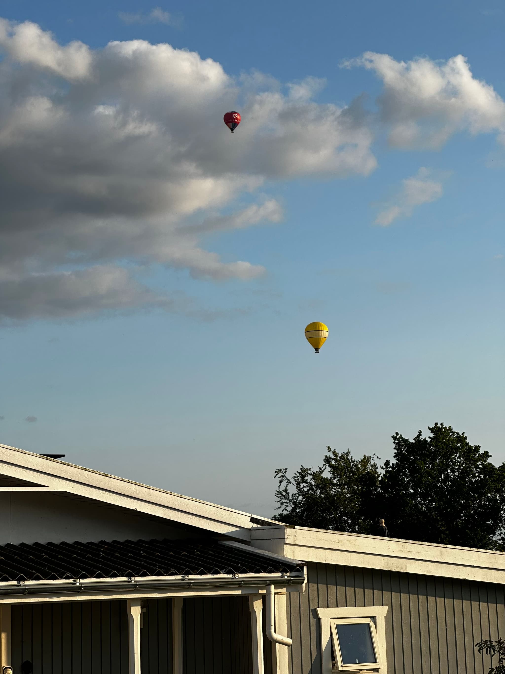 Two hot air balloons in the sky above a building with a cloudy backdrop