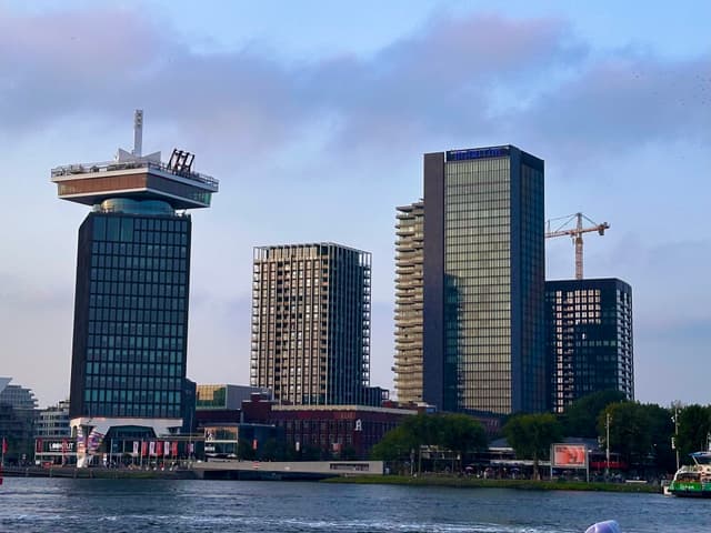 A waterfront cityscape featuring modern high-rise buildings, including a distinctive tower with a rooftop structure resembling a circular platform