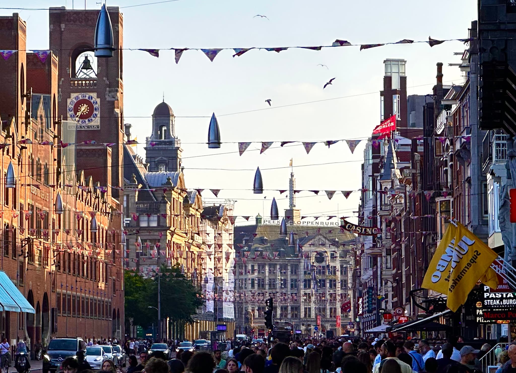 A bustling city street with historic buildings, decorative flags strung across, and a crowd of people