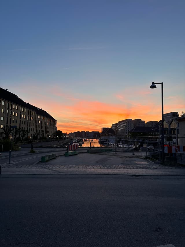 A sunset over a canal flanked by buildings, with a streetlamp silhouetted against the colorful sky