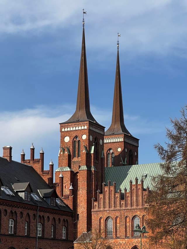 A historic brick cathedral with two tall spires under a partly cloudy sky